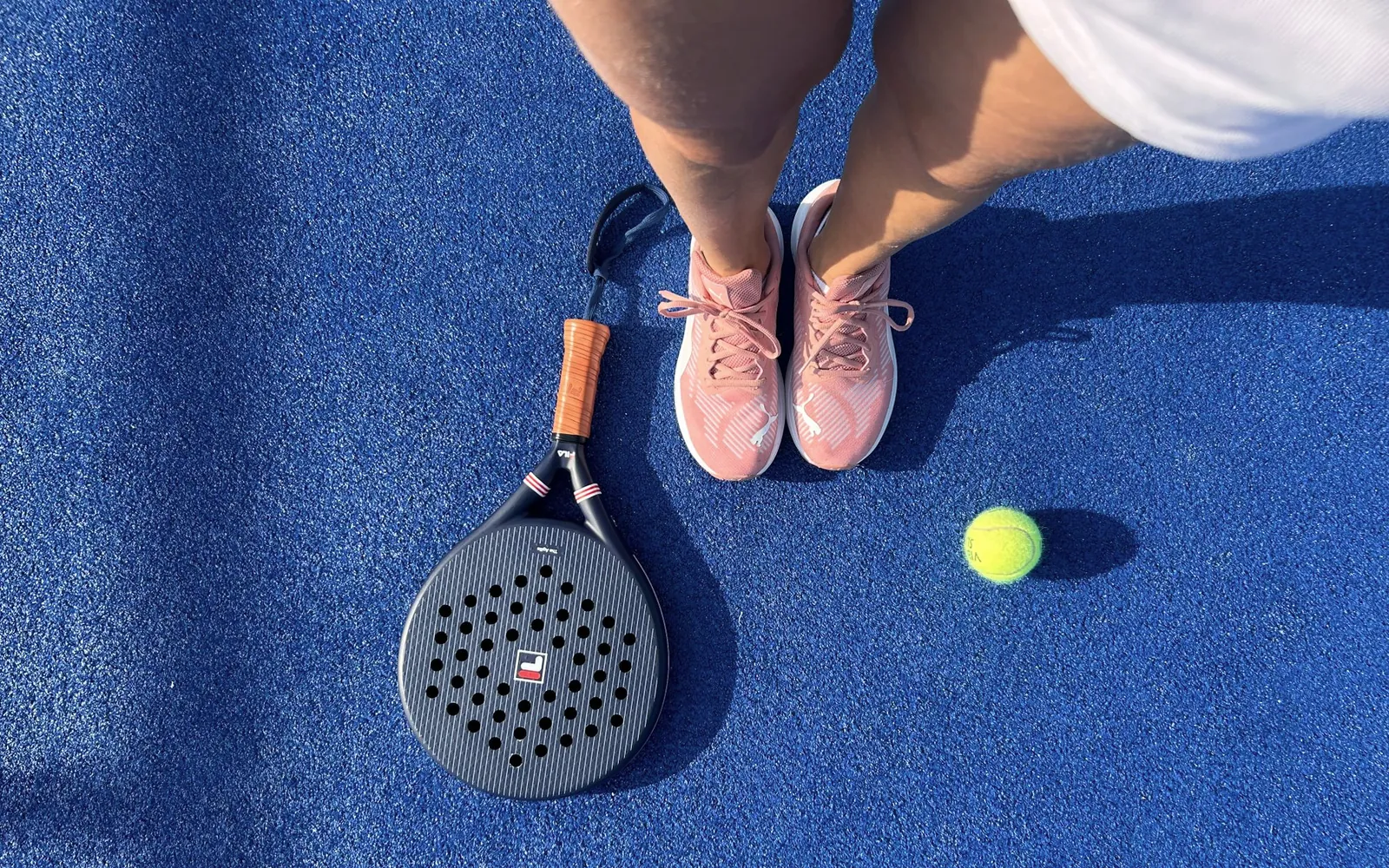 A padel racket, ball and player standing on a blue court